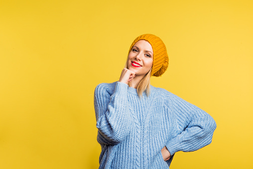 Portrait of a young beautiful woman with a woolen sweater and a hat in studio on a yellow background.