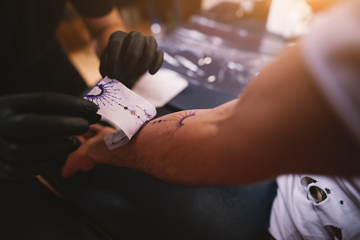 Close up of tattoo artists removing scetch sticker he previously made from customers arm.