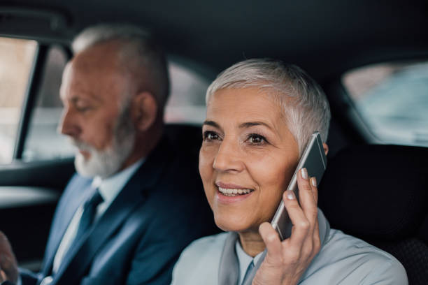 istock Business woman using phone while driving in a car with coworker 958473144