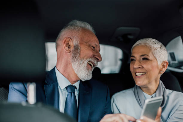 istock Senior couple using phone and smiling in a car 958473152