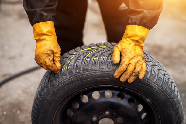 istock Mechanic with orange gloves is using chalk to mark tires while leaning on one in his workshop. 958479526
