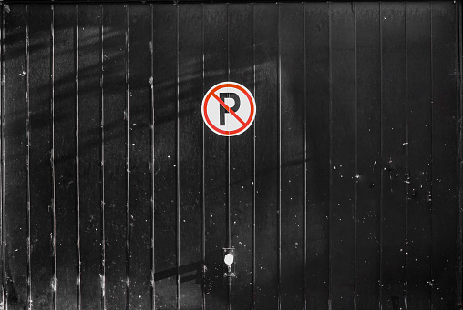Circular no car parking sign on a background of black garage door.