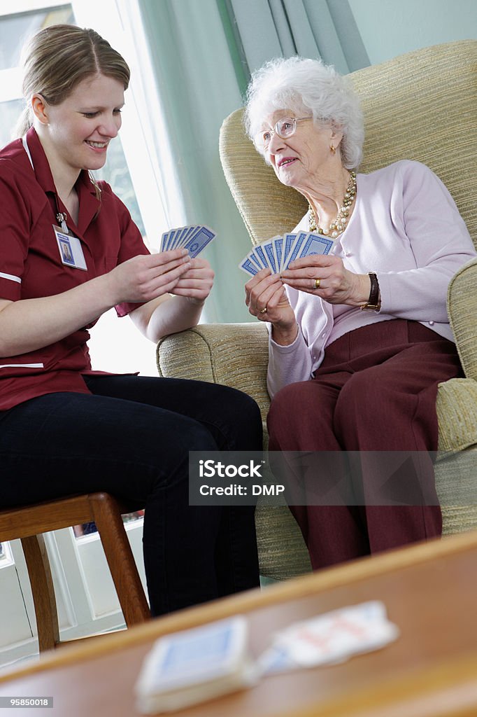 Jovem enfermeira jogando cartas com cuidados de mulher sênior em casa - Foto de stock de Brincar royalty-free