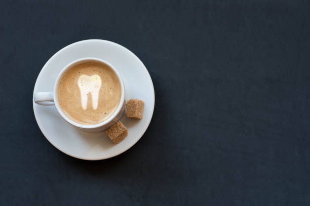 Cup of coffee with milk, cane sugar and tooth sign on dark background. Top view Copy space stock photo