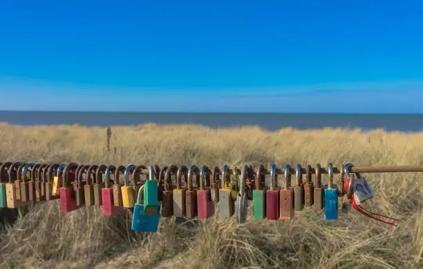 Love locks, hanging on a rusty fence at the seaside of north holland. Outlook in egmond aan zee with a romantic spot for couples in love, that seal their relationship with this Symbol.