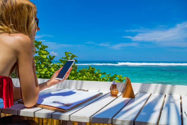 istock Girl using cellphone in the restaurant on a exotic tropical beach. 958519580