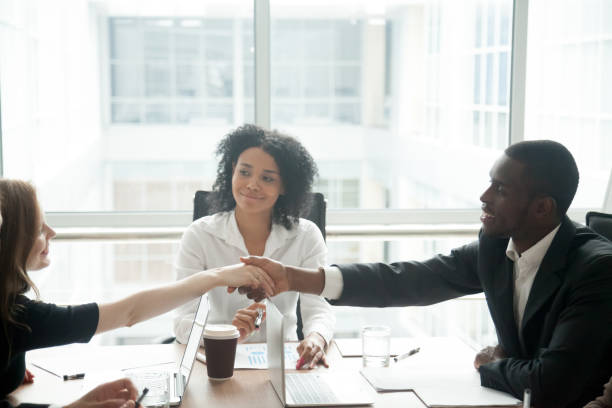 sonriendo el apretón de manos de empresario africano saludo a empresaria caucásica en reunión del grupo - mediación fotografías e imágenes de stock