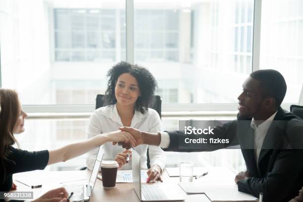 Sonriendo El Apretón De Manos De Empresario Africano Saludo A Empresaria Caucásica En Reunión Del Grupo Foto de stock y más banco de imágenes de Mediación