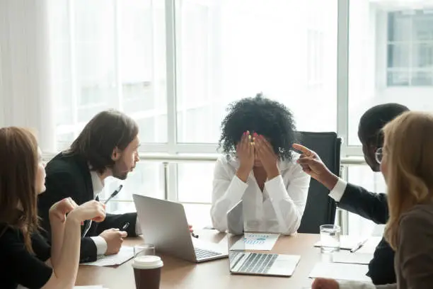 Rude diverse colleagues humiliating offending stressed upset young african woman leader suffering from gender racial discrimination during meeting or feeling exhausted tired of responsibility at work