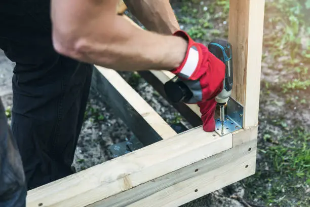 Photo of wood shed construction - man screwing corner joint brace