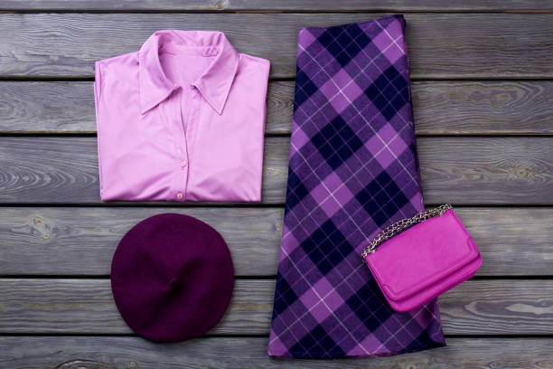Set of female elegant attire. Women purple color shirt and skirt, wooden background. Feminine fashion clutch and beret. Ladies classy apparel flat lay.