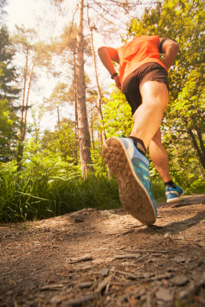 Runner in forest - low angle view Low angle view of a runner jogging in forest with a sun shining through trees. running jogging men human leg stock pictures, royalty-free photos & images