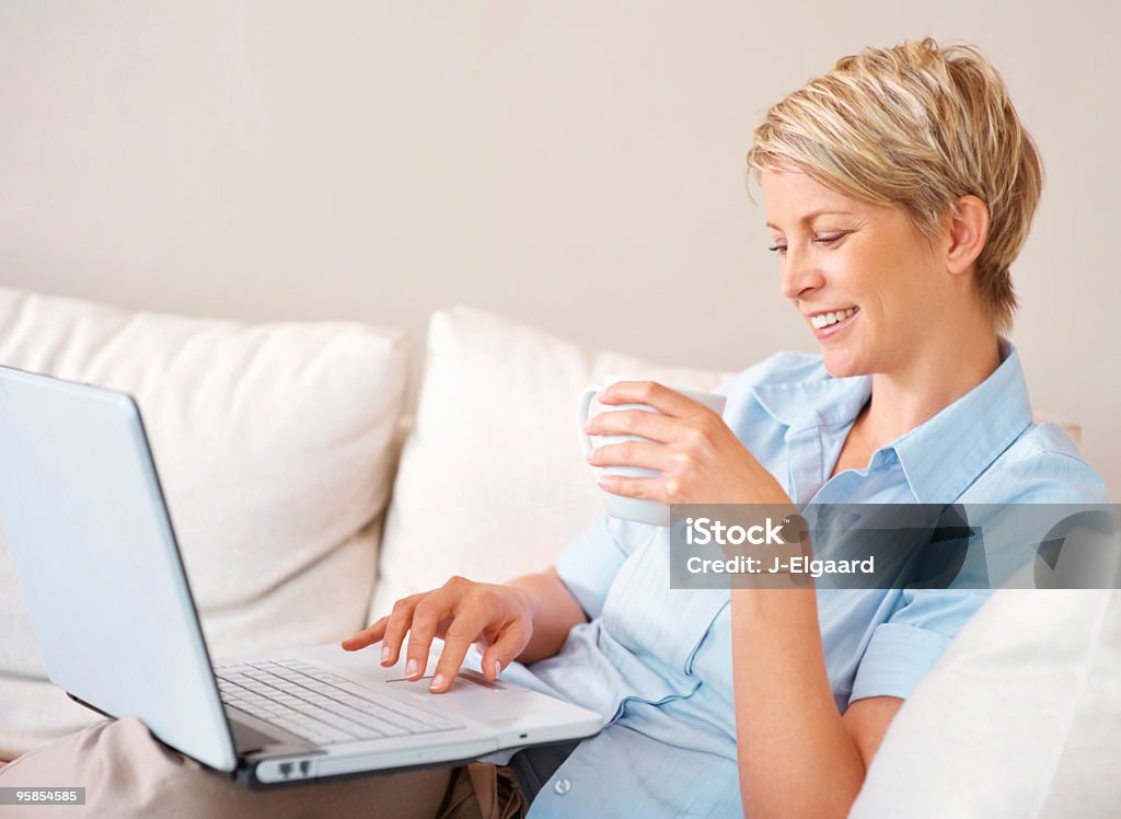 Mujer trabajando en su computadora portátil mientras disfruta de un café - Foto de stock de 30-34 años libre de derechos