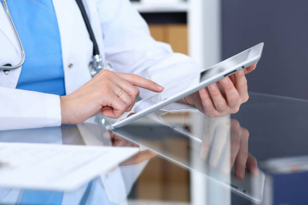istock Woman doctor using tablet computer while sitting at the glass table in hospital office, closeup. Healthcare, insurance and medicine concept 958549834