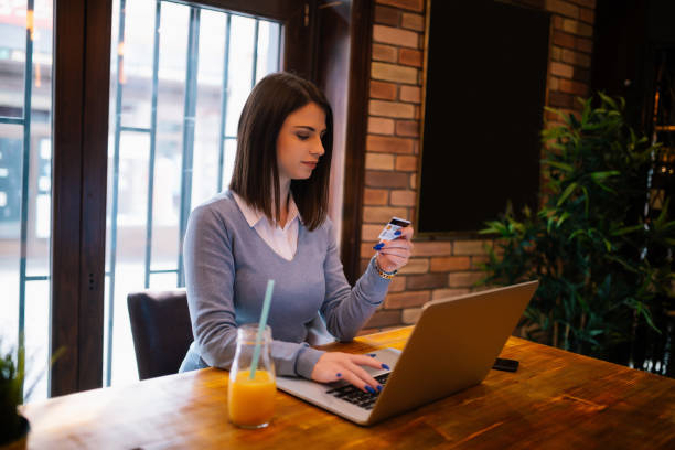 istock Young brunette drinking orange juice and making online shopping while sitting in cafe 958552350