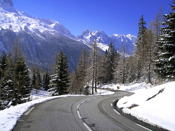 A winding mountain road with snowy mountains and evergreens stock photo