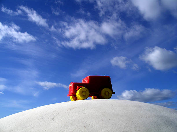 Red plastic toy car against blue sky with clouds stock photo