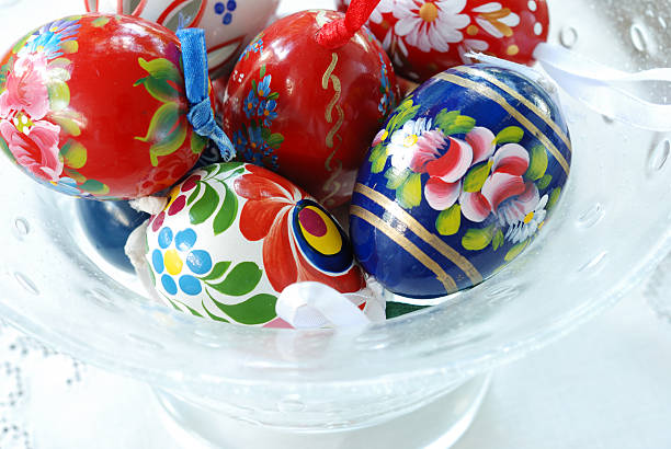 Close up of wooden eggs painted with Hungarian folk designs in a glass bowl on a white lace tablecloth. Easter decorations.