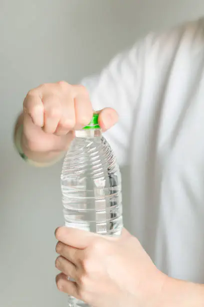 A woman in white T-shirt is opening cover of drinking water bottle.