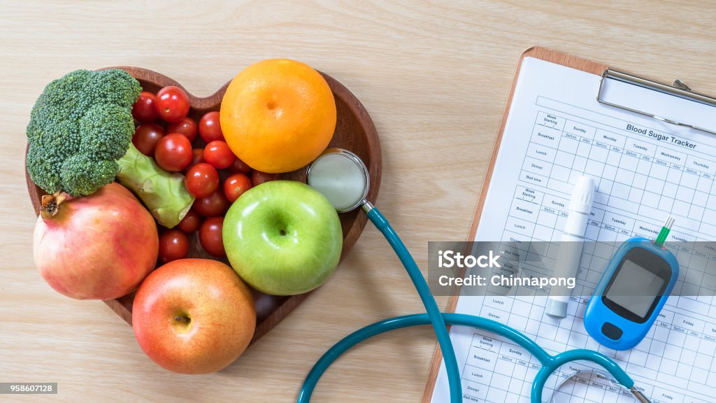 Diabetes monitor, Cholesterol diet and healthy food eating nutritional concept with clean fruits in nutritionist's heart dish and patient's  blood sugar control record with diabetic measuring tool kit Diabetes Stock Photo