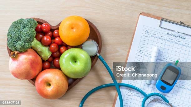 Diabetes Monitor Cholesterol Diet And Healthy Food Eating Nutritional Concept With Clean Fruits In Nutritionists Heart Dish And Patients Blood Sugar Control Record With Diabetic Measuring Tool Kit Stock Photo - Download Image Now