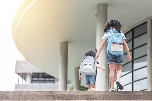 女の子の子供たち(小学生)がバックパックを持ち、学校の初日に授業に走り、楽しそうに階段を建て歩いて学校教育のコンセプトに戻る - elementary school building ストックフォトと画像