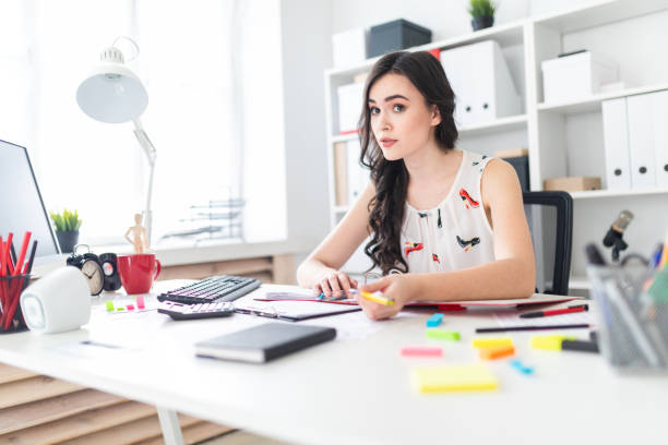 istock A beautiful young girl is sitting at the office table with documents and a pen in her hands, and is negotiating. 958607600