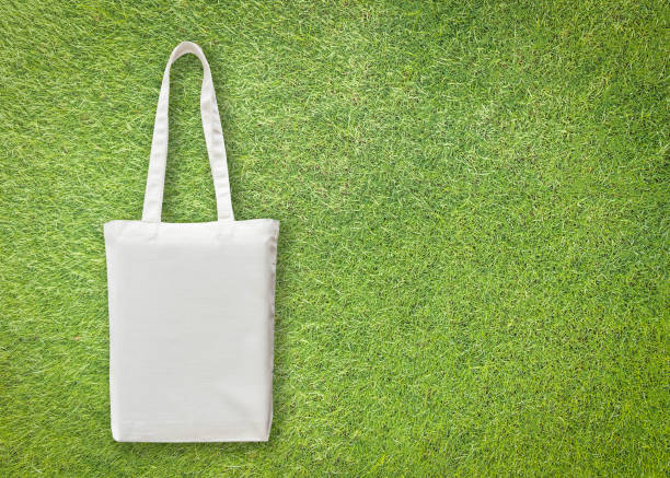 istock White cotton canvas eco shopping bag mock up with handle isolated on green grass lawn  background for handbag fashion accessory design template with go green concept 958607748