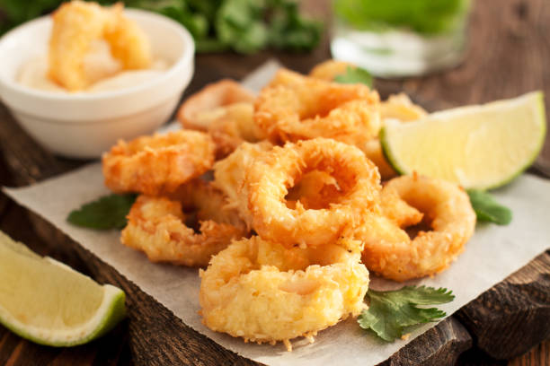 Fried calamari rings on wooden cutting board Fried squid rings on wooden cutting board with lemon and parsley calamari stock pictures, royalty-free photos & images