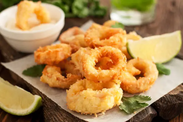 Fried squid rings on wooden cutting board with lemon and parsley