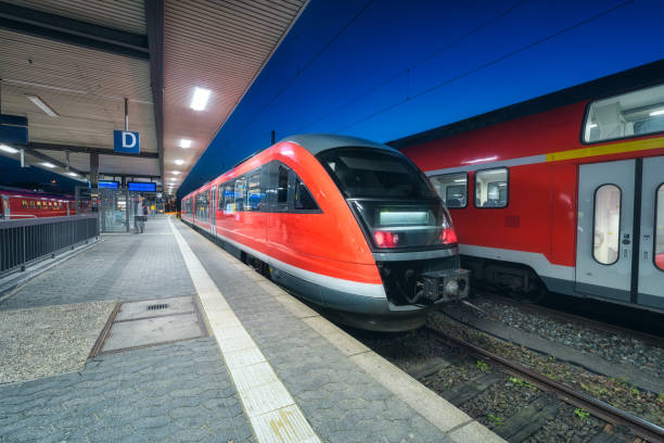 High speed train on the railway station at night in Nuremberg, Germany. Modern intercity train on the railway platform with illumintain. Commuter red train on railroad. Passenger transportation. Dusk