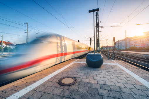 White high speed train in motion on the railway station at sunset. Germany. Blurred modern intercity train on the railway platform. Industry. Passenger train on railroad. Railway travel in Europe