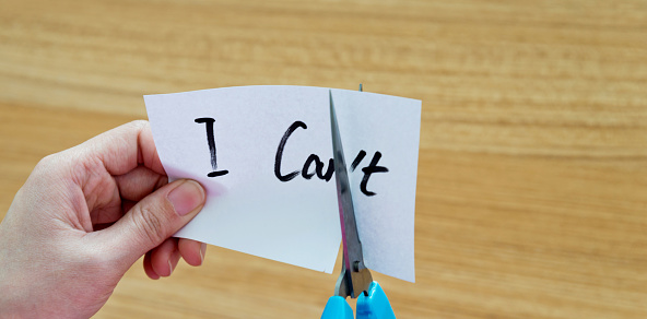 Woman hand holding scissors cutting word 'I can't'