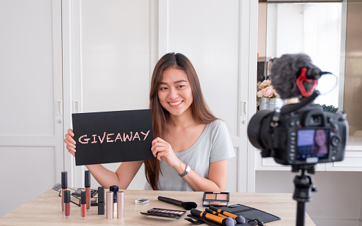 Asian young female blogger giveaway gift to fan following channel while recording vlog video with makeup cosmetic at home online influencer on social media concept.live streaming viral