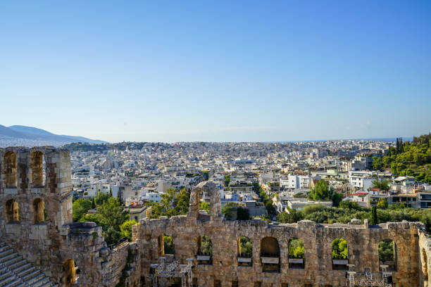 vista del paesaggio urbano di atene attraverso l'antico teatro in pietra che vede l'architettura degli edifici bianchi lowrise, la montagna, gli alberi e lo sfondo del cielo blu chiaro - clear sky acropolis athens greece greece foto e immagini stock