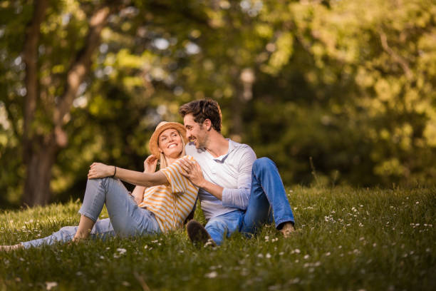 istock Young happy couple talking while relaxing in grass at the park. 958657312