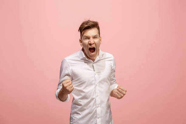istock The young emotional angry man screaming on pink studio background 958663880