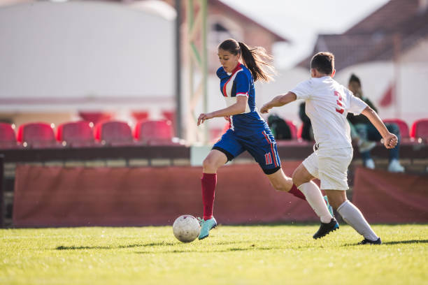 Teenage soccer player running with ball while trying to avoid her opponent on a match.