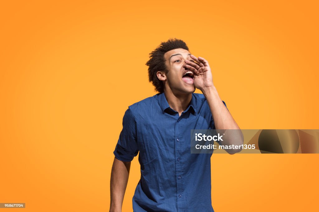 Isolated on blue young casual man shouting at studio Young afro man shouting. Crying emotional man screaming on blue studio background. Male half-length profile portrait. Human emotions, facial expression concept. Trendy colors. Shouting Stock Photo