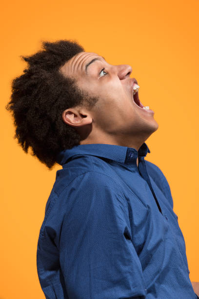 istock The young emotional angry man screaming on orange studio background 958676542