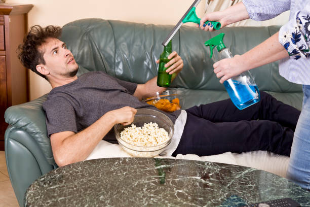 man is drinking beer and watching tv while his wife cleaning house - routine foods and drinks clothing household equipment imagens e fotografias de stock