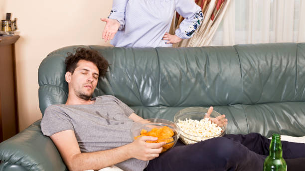 angry wife and sleeping husband on the sofa and junk food - routine foods and drinks clothing household equipment imagens e fotografias de stock