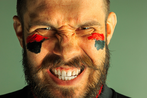 Portrait of a man with the flag of the Germany painted on him face. Young male caucasian model closeup. Football, soccer, fan concept. Human emotions, facial expressions concepts