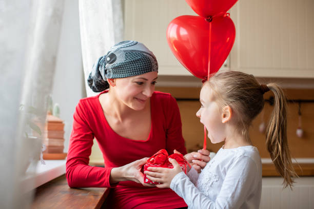 giovane madre, maestra di cancro e sua figlia carina, che festeggiano il compleanno con palloncini e regali. concetto di supporto familiare allo stile di vita. - cancer chemotherapy drug baby family foto e immagini stock