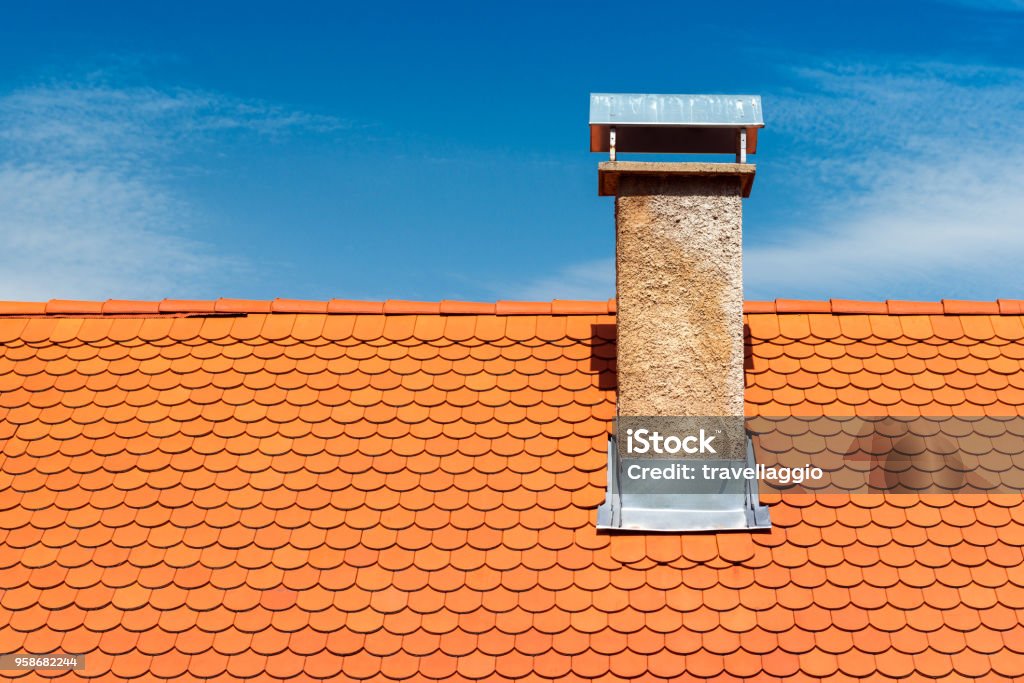 Modern roof with chimney. Orange ceramic tile, shingle. Blue sky on the background Modern roof with chimney. Orange ceramic tile, shingle. Blue sky on the background. Rooftop Stock Photo