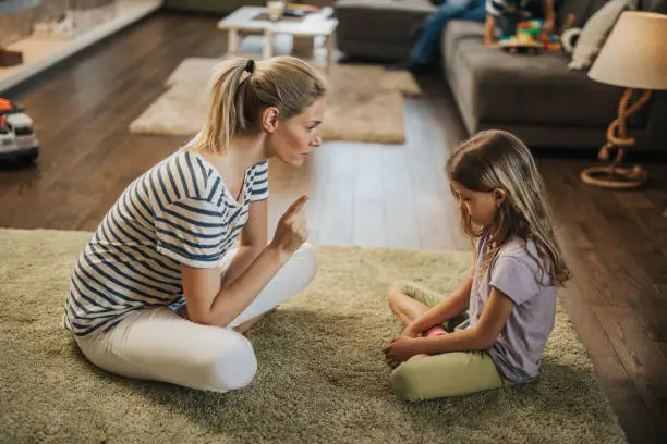 Photo of Mother scolding little girl on carpet in the living room.