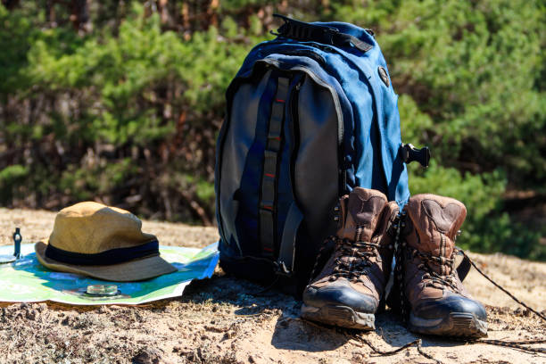 istock Tourist backpack with hiking boots, hat, compass and map on the glade in pine forest 958684278