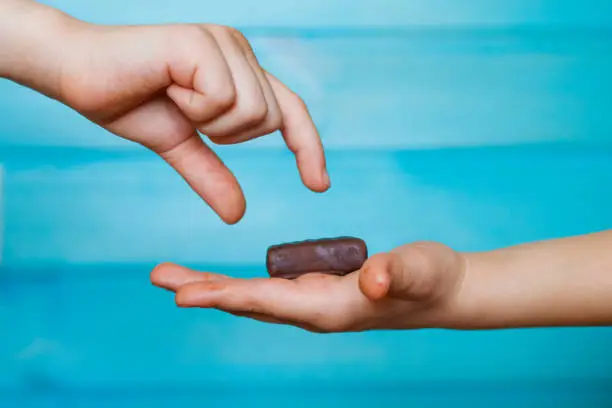 Photo of The child holds a chocolate candy in the palm of his hand, sharing it with his friend