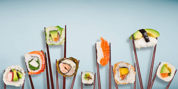 Traditional japanese sushi pieces placed between chopsticks, separated on light blue pastel background Traditional japanese sushi pieces placed between chopsticks, separated on light blue pastel background. Very high resolution image. maxi length stock pictures, royalty-free photos & images