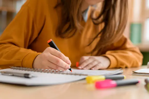 Photo of Young unrecognisable female college student in class, taking notes and using highlighter. Focused student in classroom. Authentic Education concept.